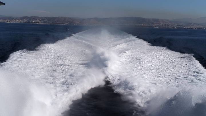 High-speed ferry wake carving white trail through deep blue sea toward distant coast.