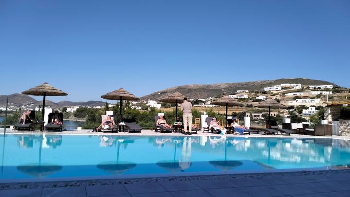 Guests lounging by infinity pool with whitewashed village and hills behind.
