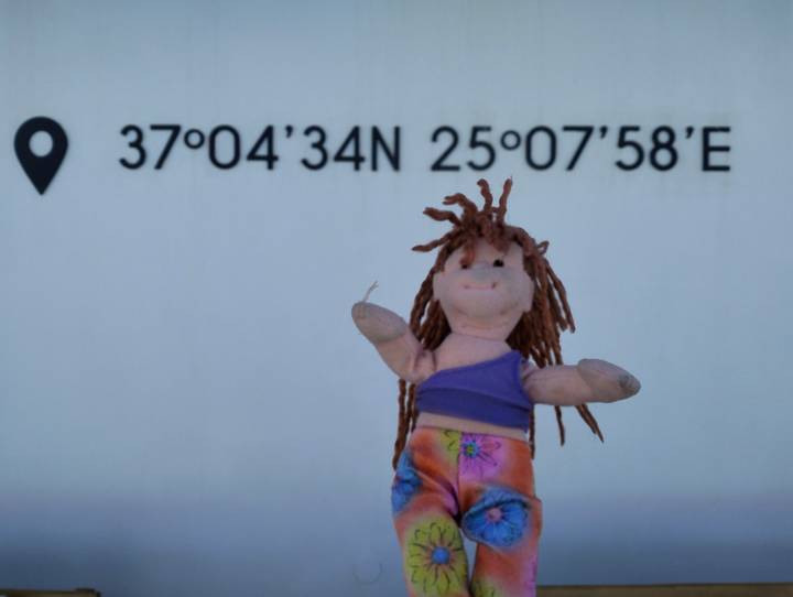 Toy doll posed in front of wall showing latitude and longitude coordinates.