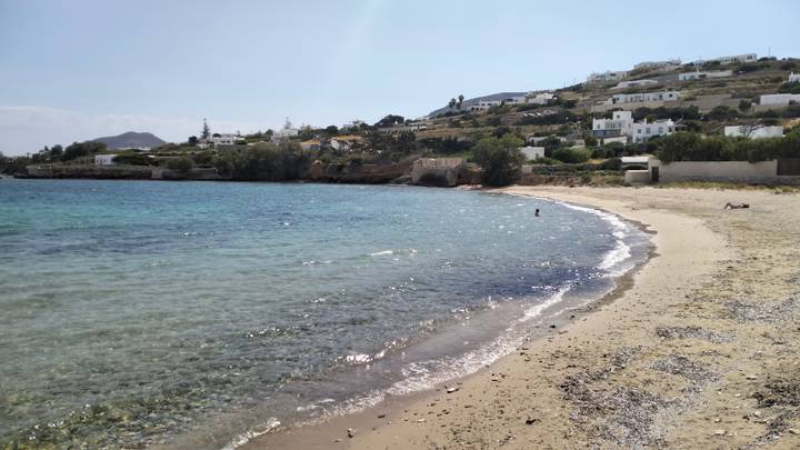 Quiet sandy beach with shallow turquoise water and white houses on hill.