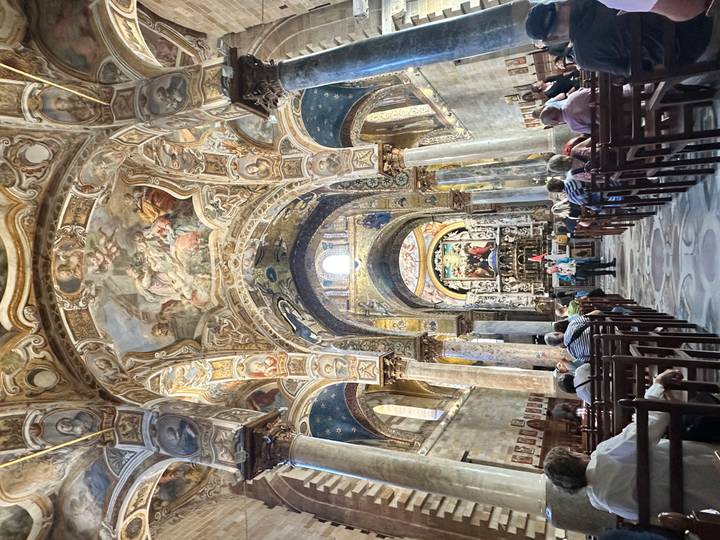 Congregation seated inside an elaborately decorated cathedral lined with gold mosaics and frescoes.