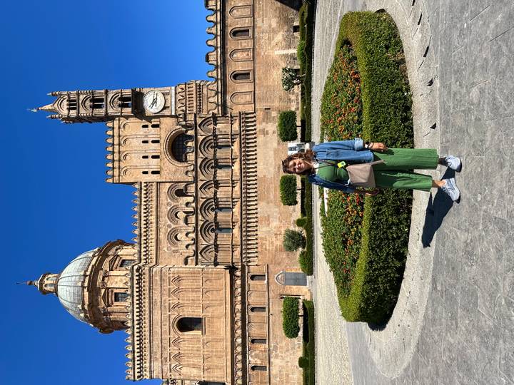 Traveler posing in front of the ornate façade of Palermo Cathedral on a clear day.