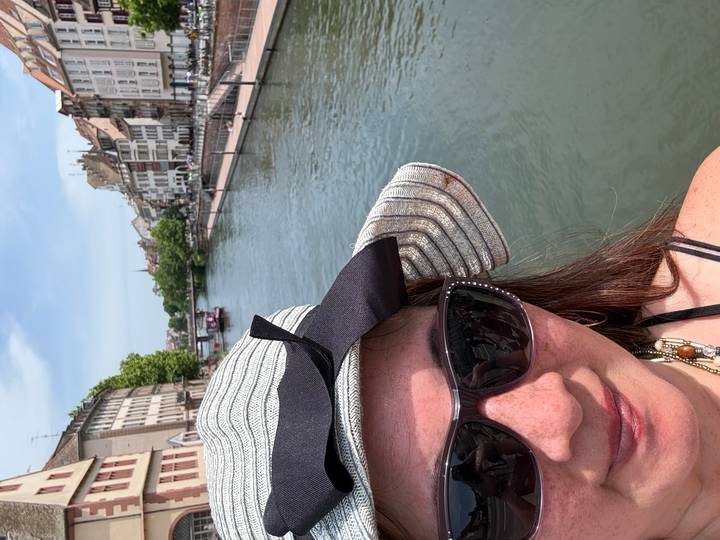 Partial selfie of a woman in sunglasses by the canal and historic houses of Strasbourg.