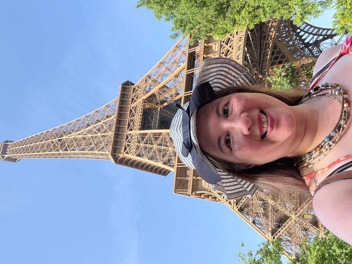 Smiling traveler taking a selfie beneath the Eiffel Tower on a clear blue day.