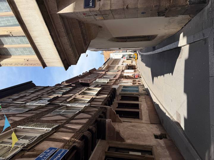 Narrow cobblestone street flanked by half-timbered medieval houses with shuttered windows under a blue sky.