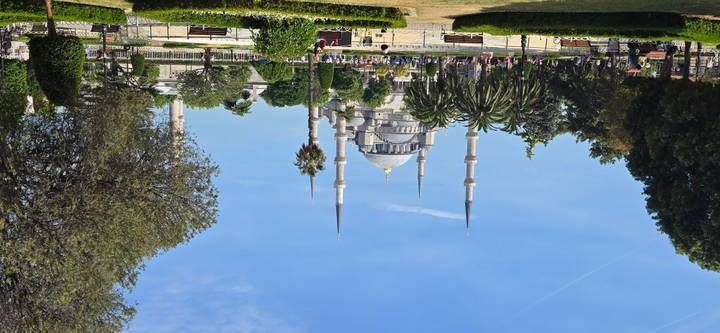 Blue Mosque rises above landscaped gardens and palm trees under a clear sky.