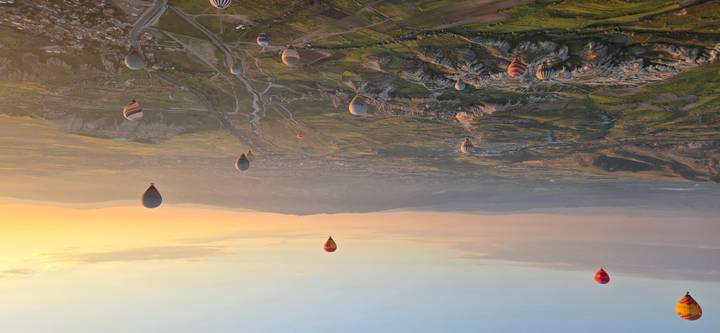 Dozens of hot-air balloons drift over Cappadocia’s valleys at sunrise.