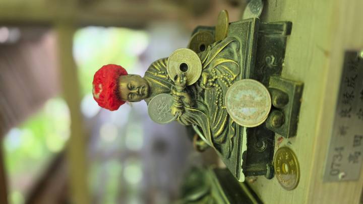 Small Buddha statue with red knitted cap surrounded by coins and offerings