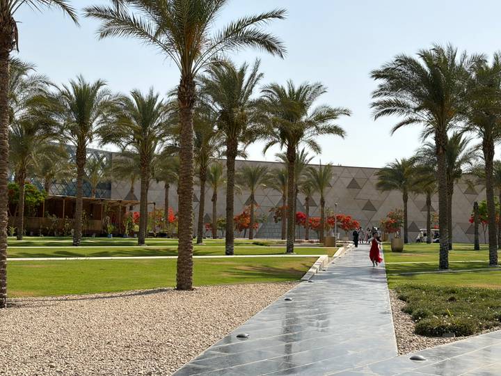 Landscaped gardens with palm trees outside a modern geometric-patterned museum in Giza.