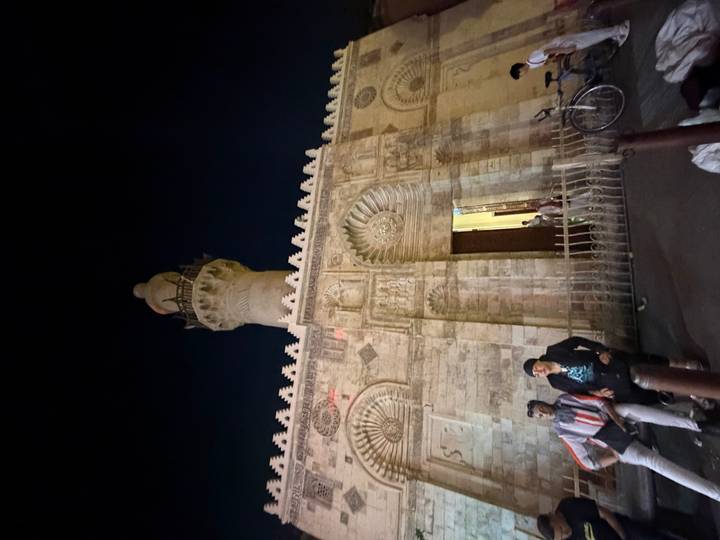 Nighttime street scene with two men sitting near a historic mosque and minaret in Cairo.