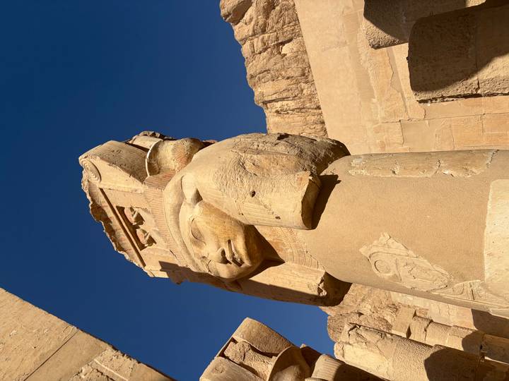Close-up of Hathor-headed column statue at the Temple of Hatshepsut against a blue sky.