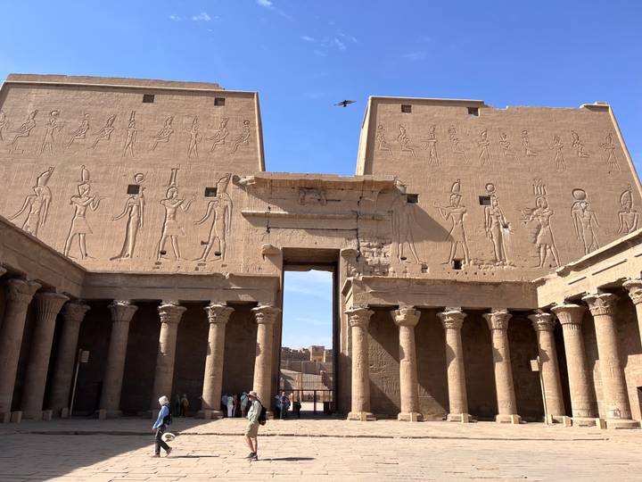 Visitors stand before towering pylons covered in hieroglyphics at an ancient temple.