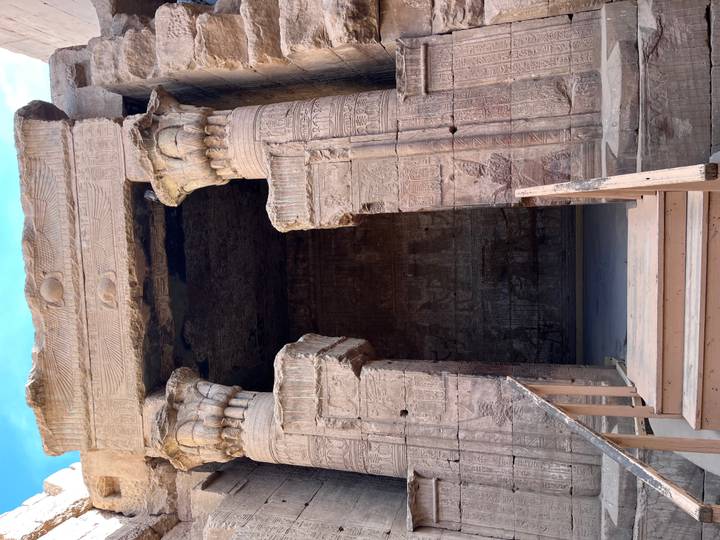 Entrance to a dimly lit ancient chamber flanked by carved columns with wooden steps leading up.