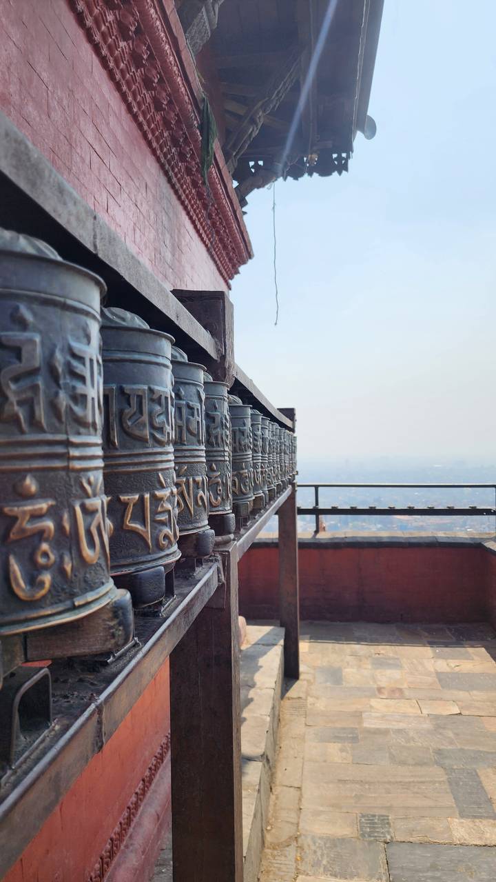 Close-up row of bronze prayer wheels in a Himalayan temple overlooking a hazy valley