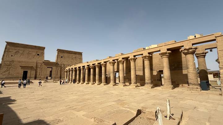 Open courtyard of an ancient Egyptian temple lined with tall stone columns under a clear sky.