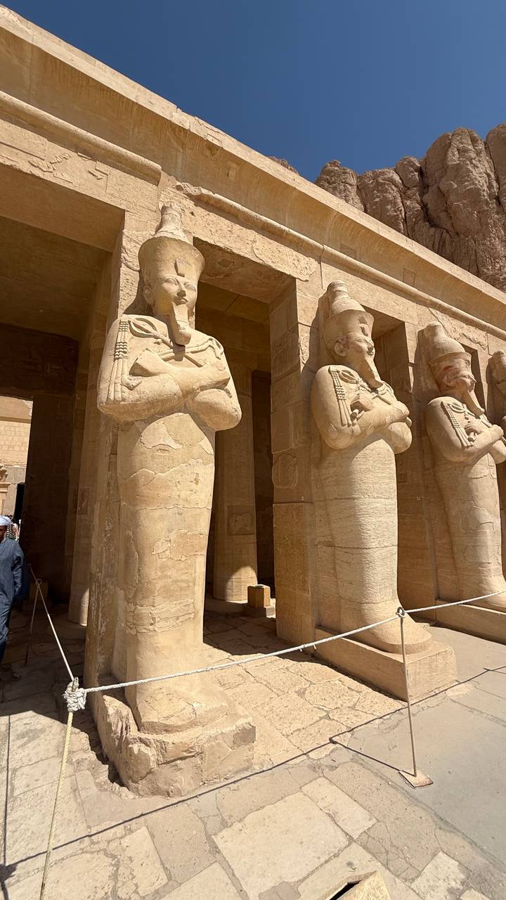 Row of monumental standing statues with crossed arms inside an ancient temple hall.