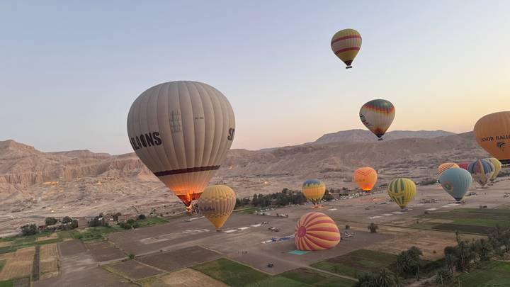 Colorful hot-air balloons rising over the Nile Valley at dawn with desert hills beyond.