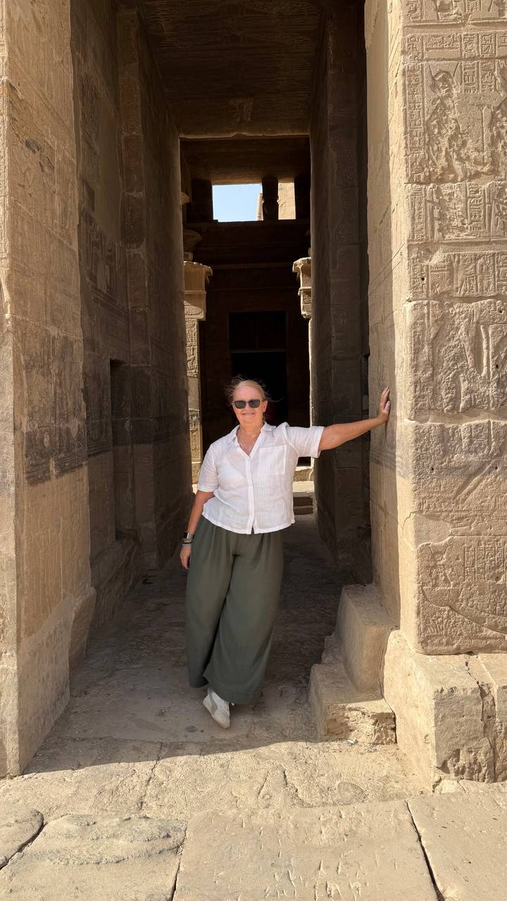 Woman leaning casually in the shaded doorway of an ancient stone temple.