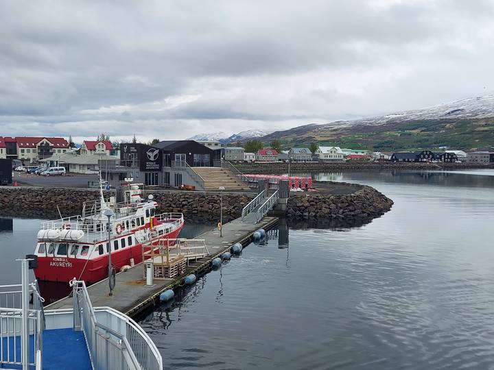 Quiet harbor scene with red patrol boat and colorful houses backed by snowy hills.
