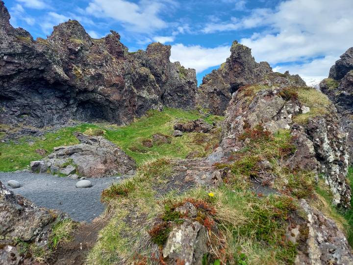 Rugged volcanic rock formations with patches of bright green moss under a blue sky.