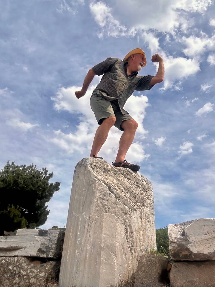Adventurer balancing on a marble ruin block against a blue sky with scattered clouds.