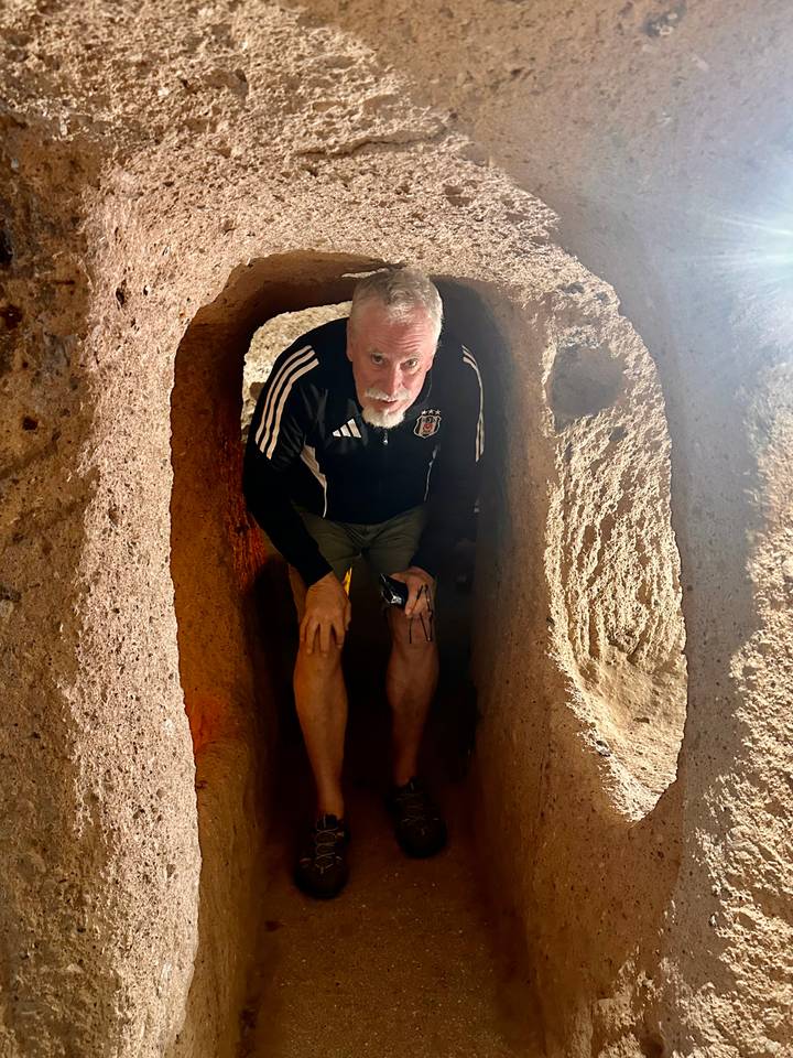Visitor crouching in a narrow tunnel of an underground city carved from reddish rock.