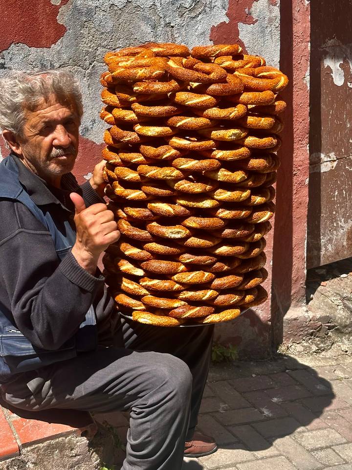 Street vendor proudly holding a towering stack of golden simit bread rings.