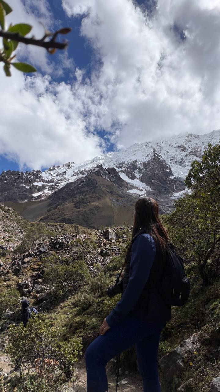Female trekker gazes at snow-covered Andean peaks and glaciers beneath a bright sky.