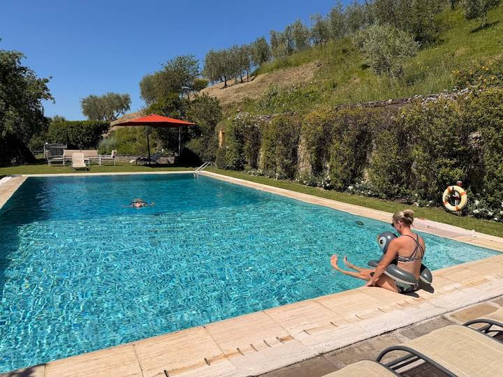 Sunny outdoor pool in a hillside garden setting with a swimmer and woman relaxing at the edge