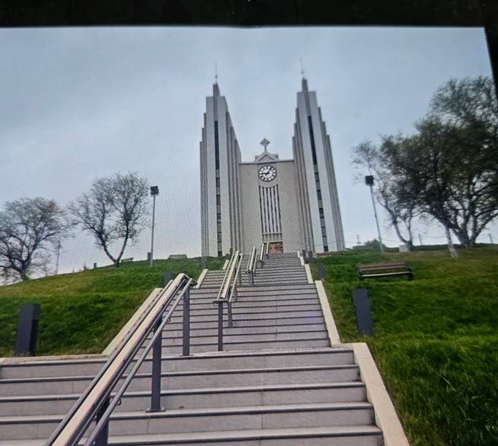 Steep staircase leading up to the modernist Akureyri Church crowned by a clock tower on a grassy hill.