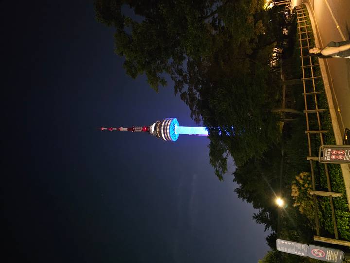N Seoul Tower glows blue and red against a dark night sky with a passer-by in the corner.