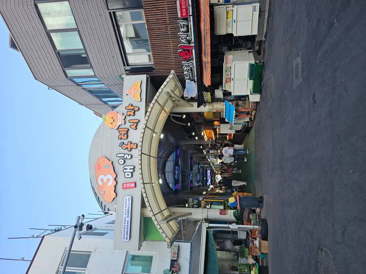 Entrance archway of a bustling Korean market with shoppers walking under colorful signage.