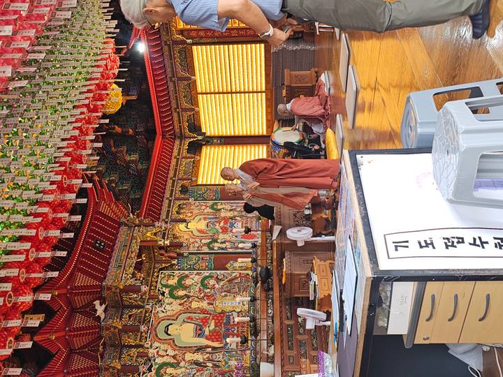 Monks chant inside an ornately decorated temple hall filled with lanterns and Buddhist art.