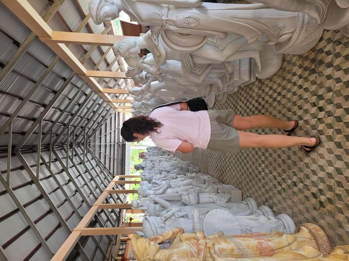 Visitor walking through a workshop lined with white marble statues under a metal roof.