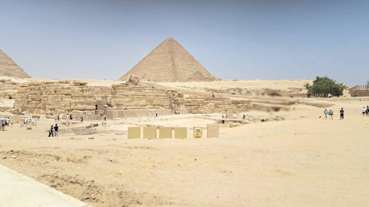 Desert panorama of the Great Pyramid of Giza with tourists exploring the foreground ruins.