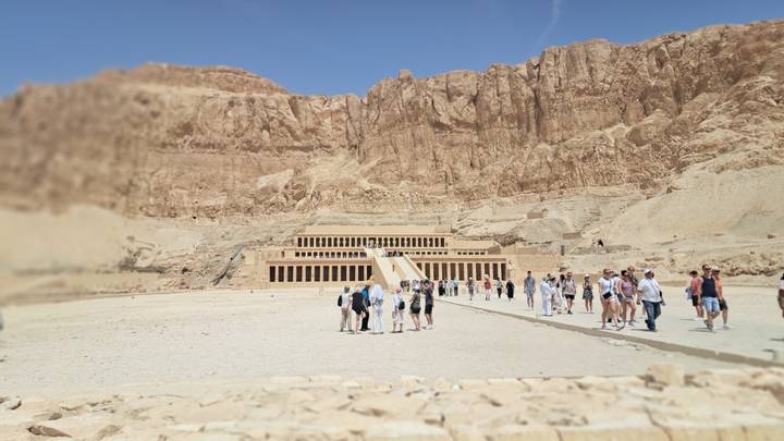 Temple of Hatshepsut dwarfed by sheer cliffs with visitors walking the grand causeway.