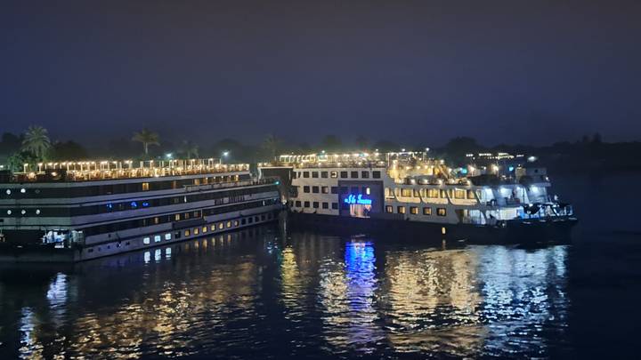Nile cruise ships moored side by side, deck lights reflecting on the dark river at night.