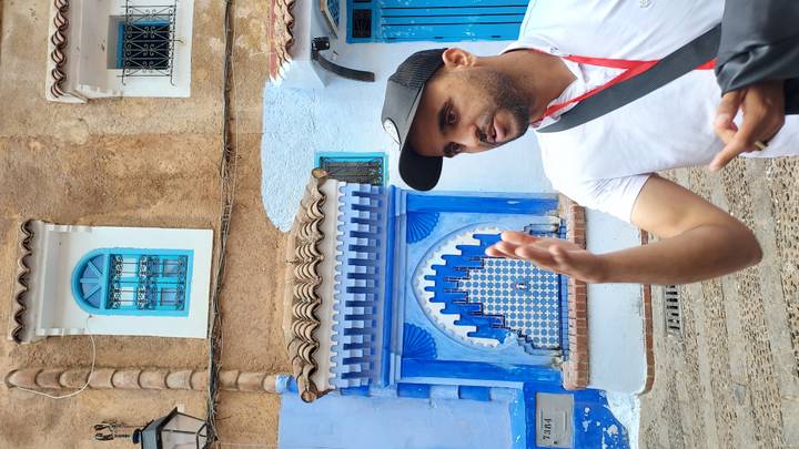 Local guide gesturing while explaining in front of the blue-painted walls and ornate doorway of Chefchaouen.