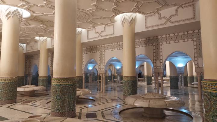 Elegant interior ablution hall of the Hassan II Mosque with ornate columns, mosaics and marble fountains softly lit.