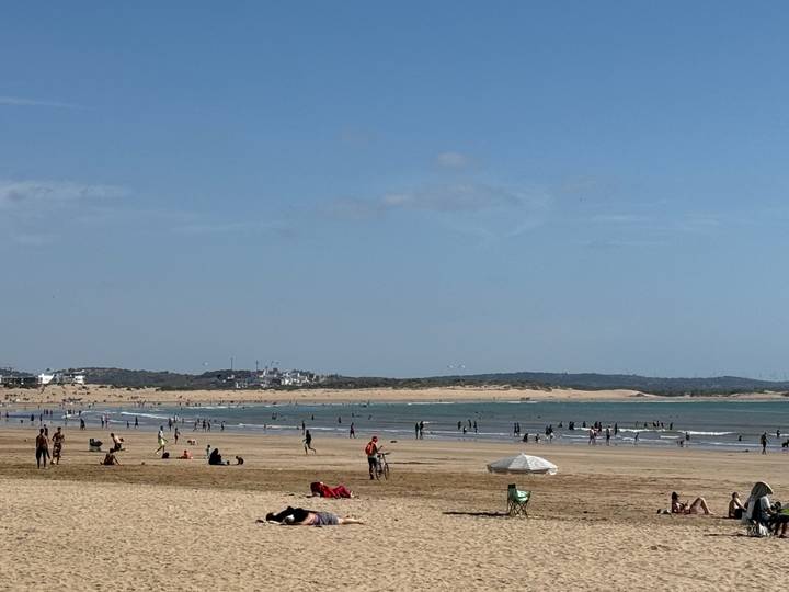 Wide sandy beach with swimmers, kite surfers and sunbathers along a calm Atlantic shoreline.