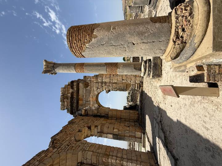 Ancient Roman archway and standing columns of Volubilis ruins under a clear blue sky.
