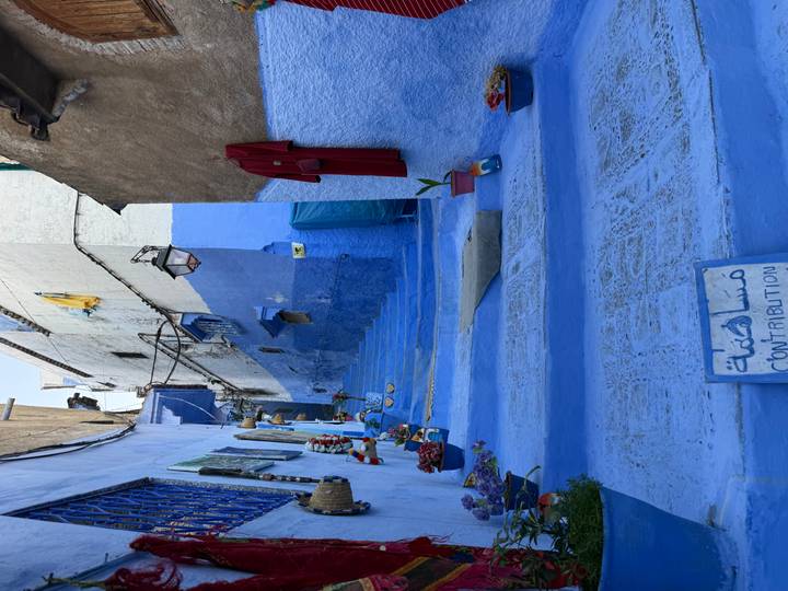Narrow blue-painted lane in Chefchaouen decorated with flowers and handicrafts.