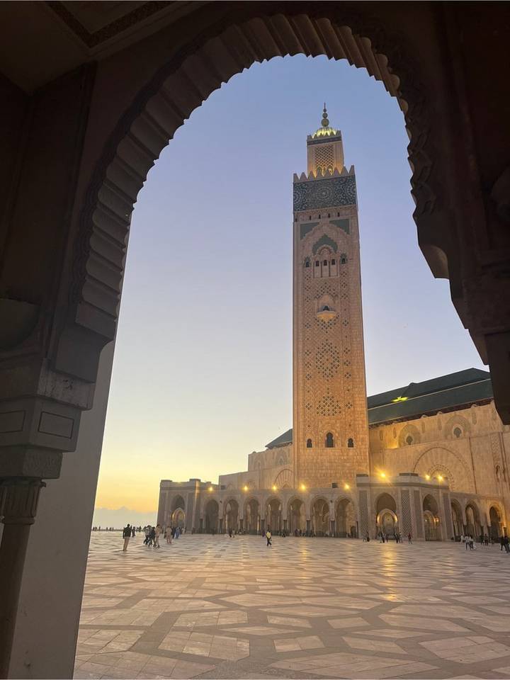 Tall minaret of Hassan II Mosque framed by archway at twilight.