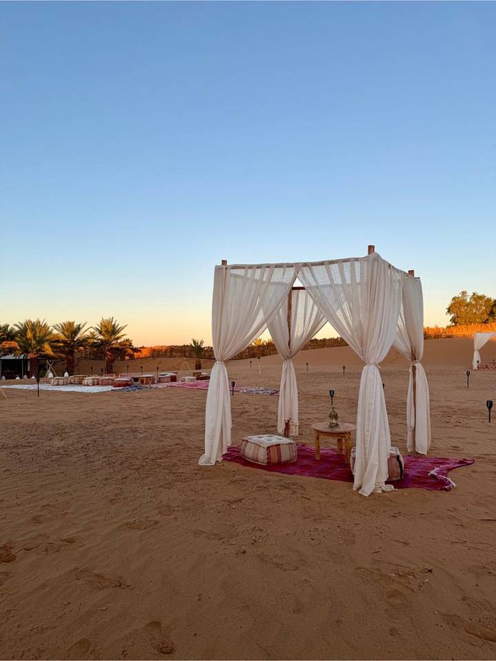 Desert lounge area with white draped canopy and low tables set for relaxation at twilight.