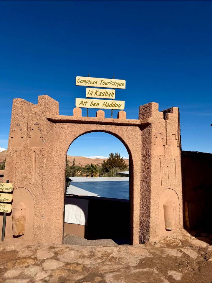 Arched adobe gateway announcing Kasbah Ait Ben Haddou against clear blue sky.