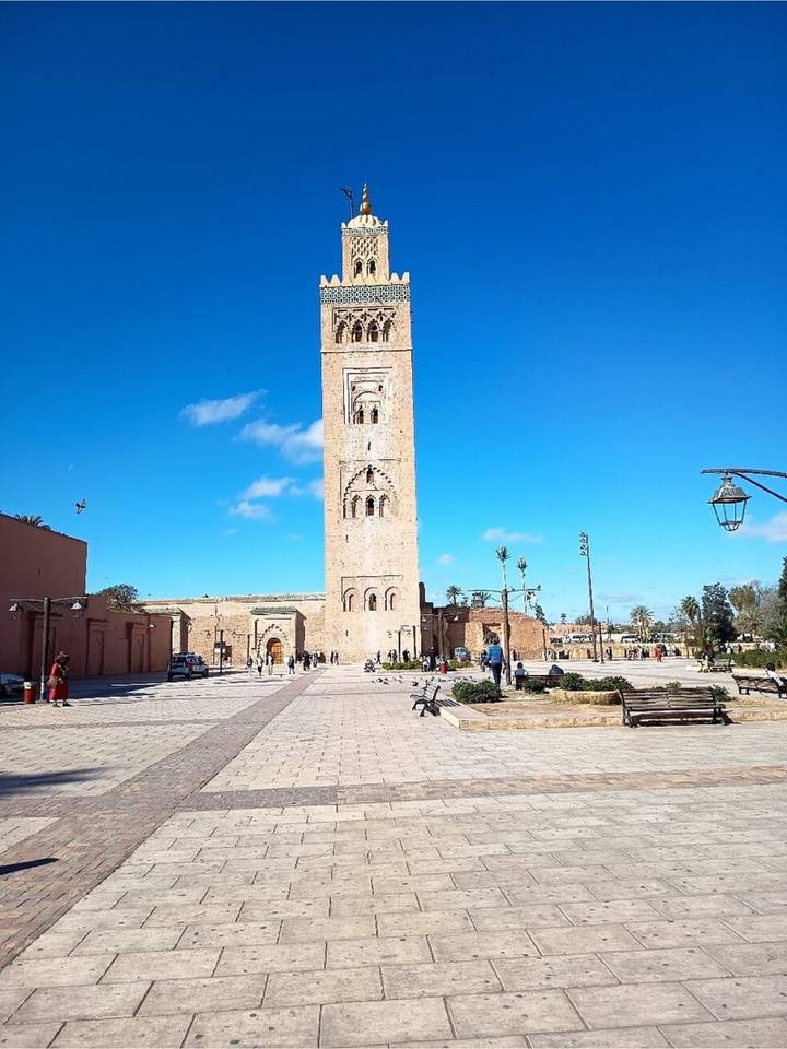 Wide plaza with the tall sandstone Koutoubia Mosque minaret rising against a bright blue sky in Marrakesh