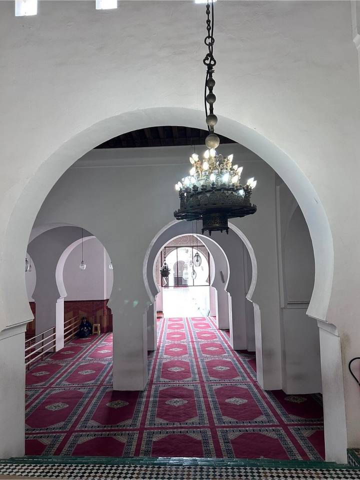 Elegant whitewashed arches and ornate chandelier inside a Moroccan mosque with patterned red carpet