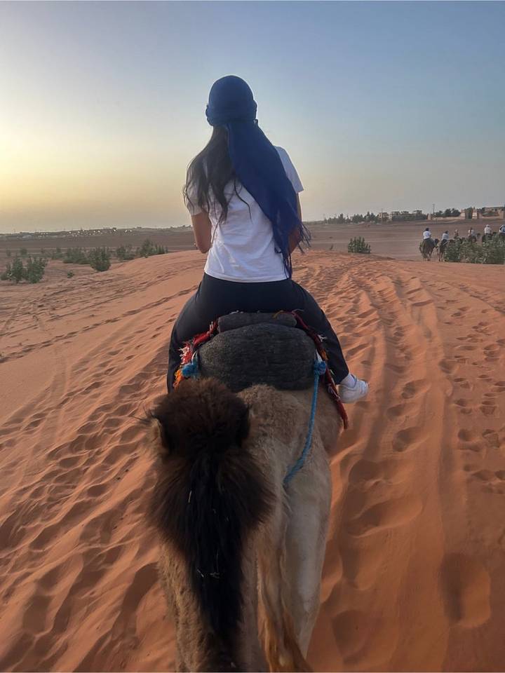 View from atop a camel as a rider leads a caravan across soft desert sand at dusk