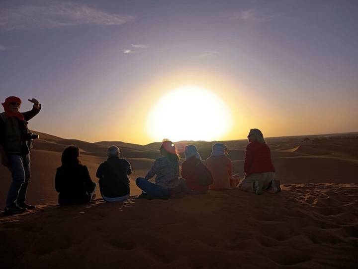 Group of travelers seated on a dune enjoying a brilliant desert sunset
