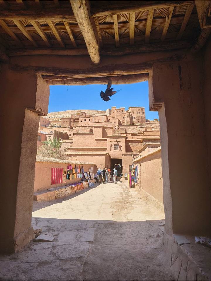 View through an adobe archway onto the fortified ksar of Ait Benhaddou with a bird in flight overhead